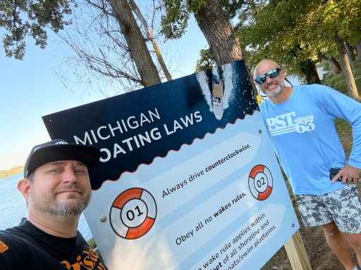 Two men beside a sign about Michigan dating laws near a lake.